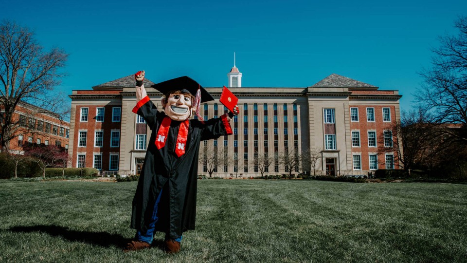 Mascot Herbie Husker holds a diploma.