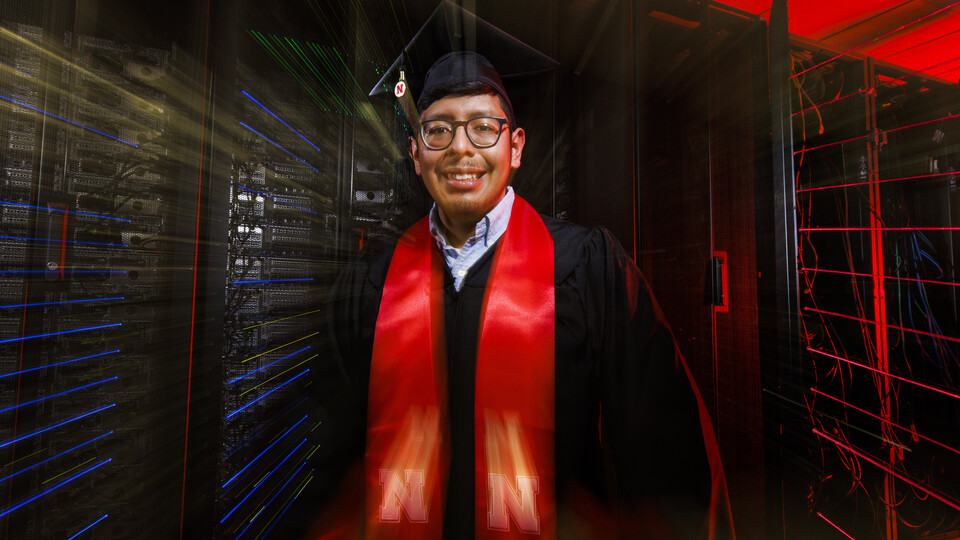 Bryan Chavez, a first-generation student who graduates Dec. 18 with degrees in computer science and mathematics, stands in front of a supercomputer in the Holland Computing Center. 