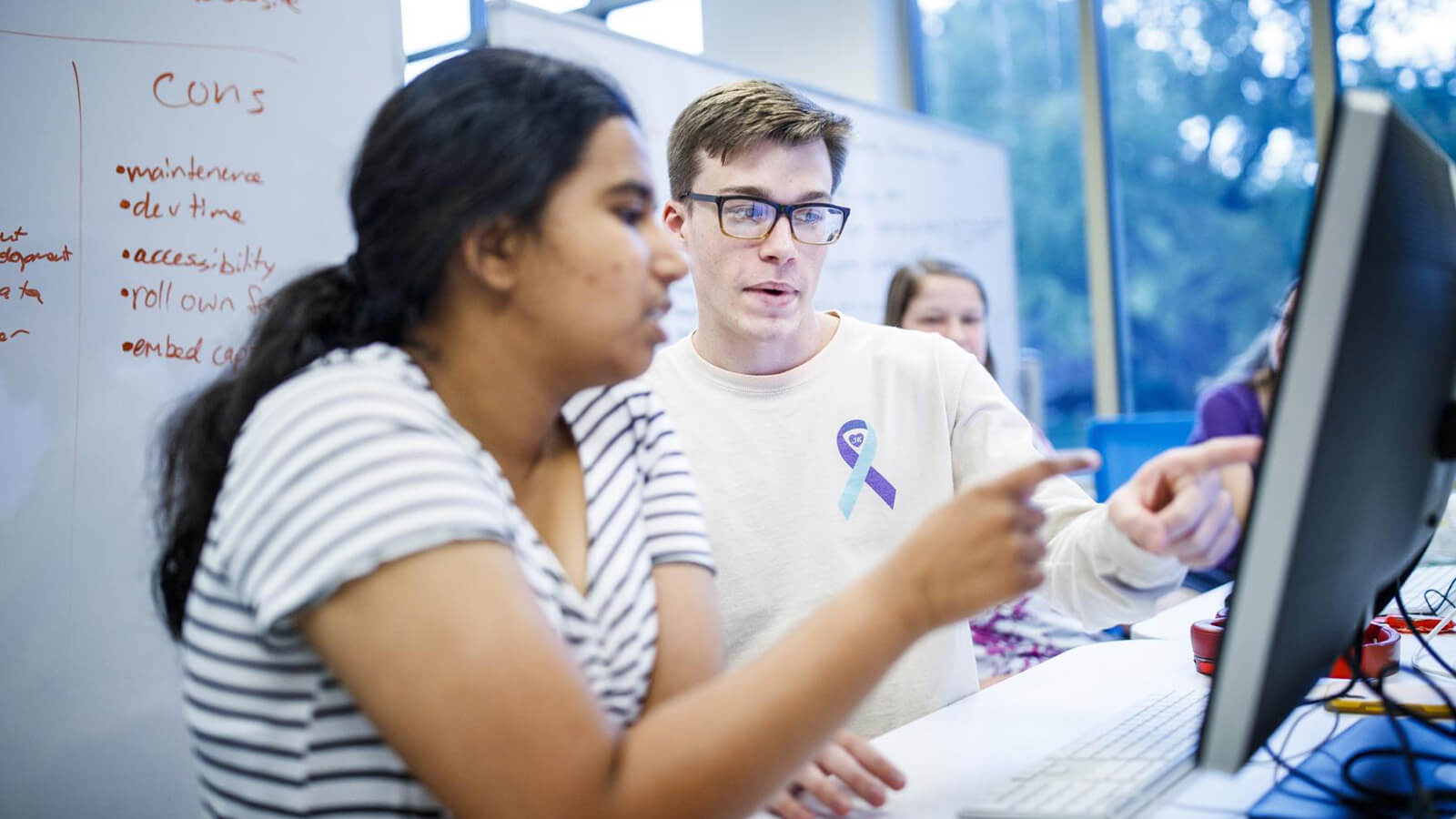 A woman and man point at computer monitor.