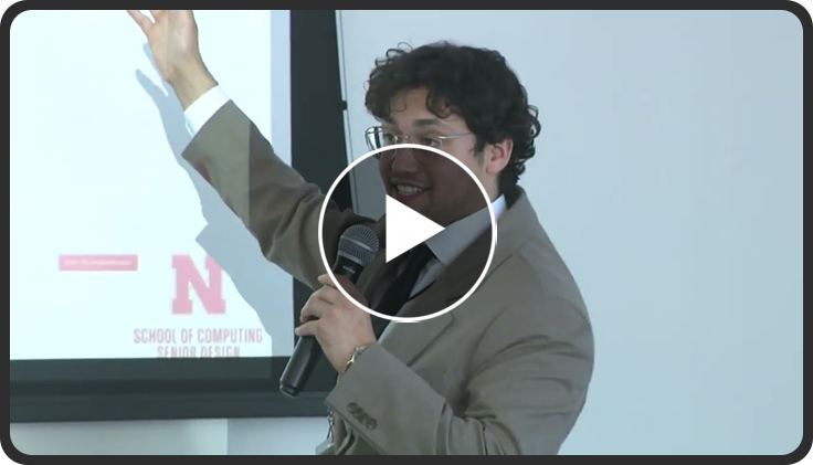 Speaker in a suit gesturing toward a presentation slide with a red "N" logo.