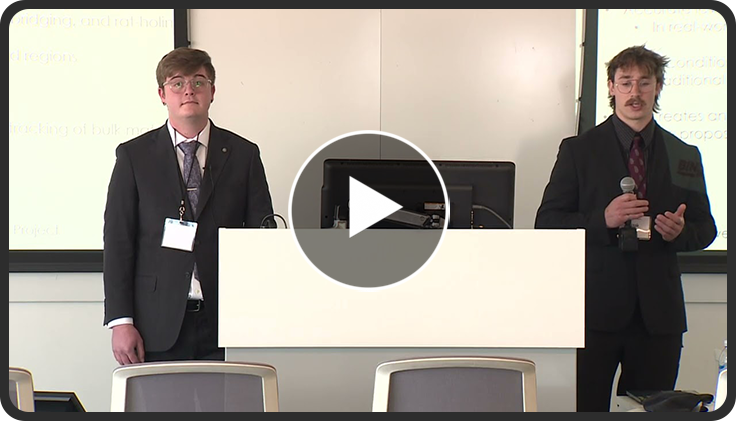 Two individuals in suits presenting at a conference podium with a projector screen behind them.