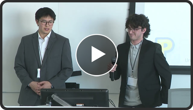 Two people in suits presenting in a conference room with a projector screen in the background.