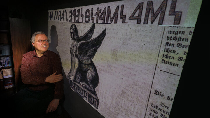 Peter Revesz poses in front of artwork of an ancient sphinx with an inscription that he deciphered.