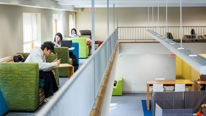 Three students sit in green booths on the balcony of the mezzanine area in Love Library South.