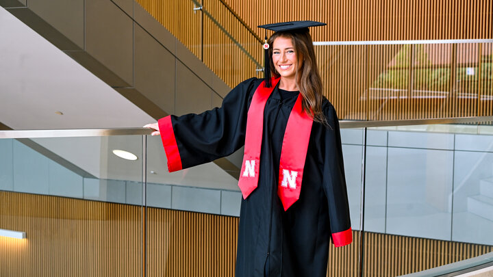 Lena Lankas stands in her cap and gown in the College of Business stairway.