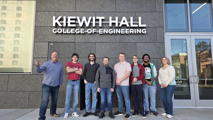 Group of eight people standing outside Kiewit Hall, College of Engineering, against a gray building.