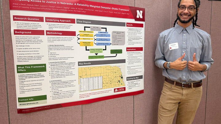 Armon'e Dean stands with his research poster in front of a beige partition wall and gives a thumbs-up.
