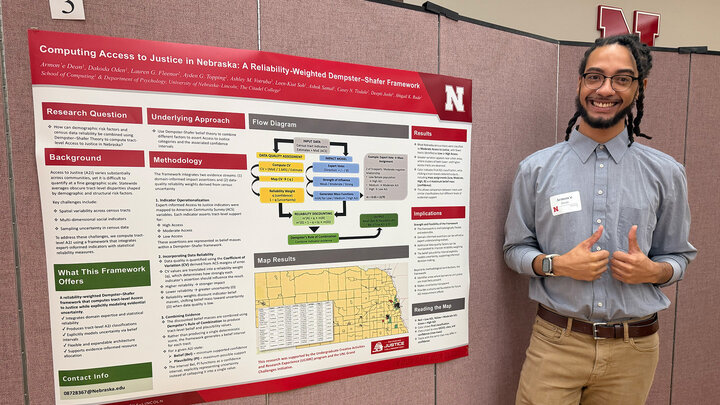 Armon'e Dean stands with his research presentation poster and gives two thumbs up.