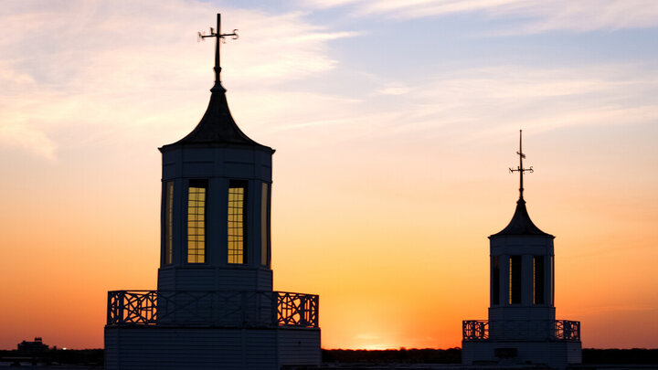 Two silhouetted towers with crosses at sunset, orange sky fading to blue.
