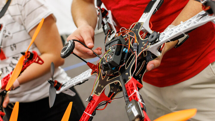 Person assembling a red and white drone with orange propellers indoors.